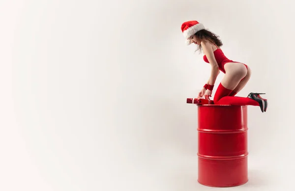 赤い樽の上にクリスマスの贈り物と白い背景を持つ赤いサンタの帽子の女性 — ストック写真