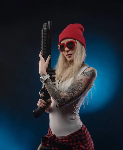 一个戴着红色帽子 深色背景上拿着猎枪的金发美女 — 图库照片