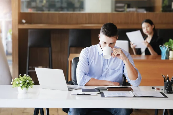 Male marketing managers drink coffee while working to reduce drowsiness before using computers, iPads, and marketing analysis papers
