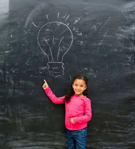 Uśmiechający Się Mała Dziewczynka Wskazując Rysowane Lampie Tablica — Zdjęcie stockowe