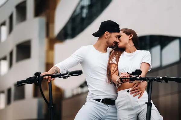 A girl and a guy are walking on electric scooters around the city, a couple in love on scooters