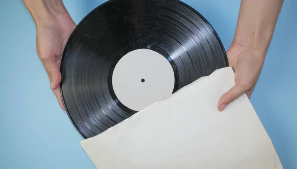 Hands hold an old vinyl record in an old paper case on a light blue background.