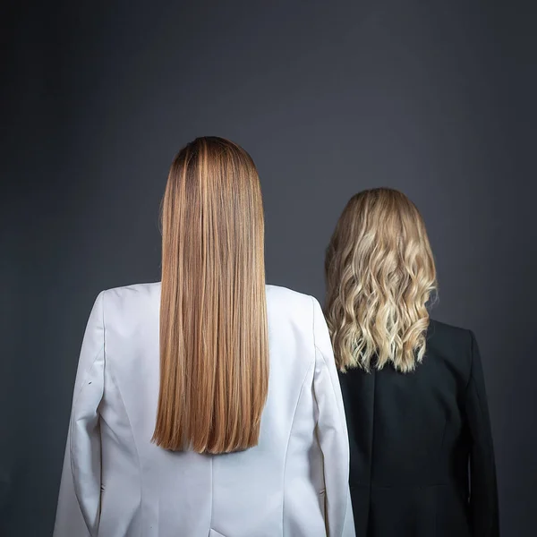 Две Девушки Длинными Светлыми Волосами Стоят Напротив Стены Строгих Костюмах — стоковое фото