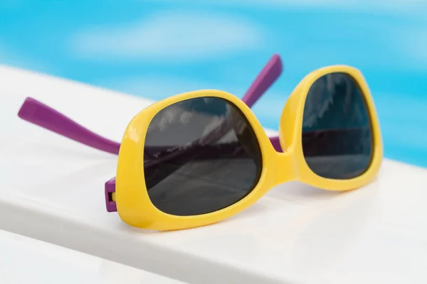 Okulary Przeciwsłoneczne Dla Dzieci Leżące Leżaku Niebieskim Tle Wody — Zdjęcie stockowe
