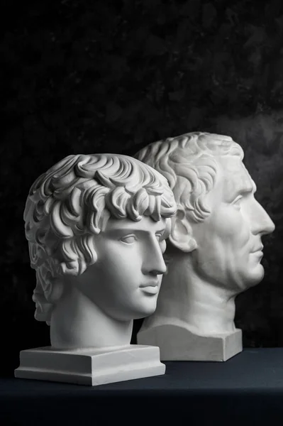 古雕像奥古斯都和安提努斯头的石膏复制品在黑暗的纹理背景 石膏雕塑人的脸 — 图库照片