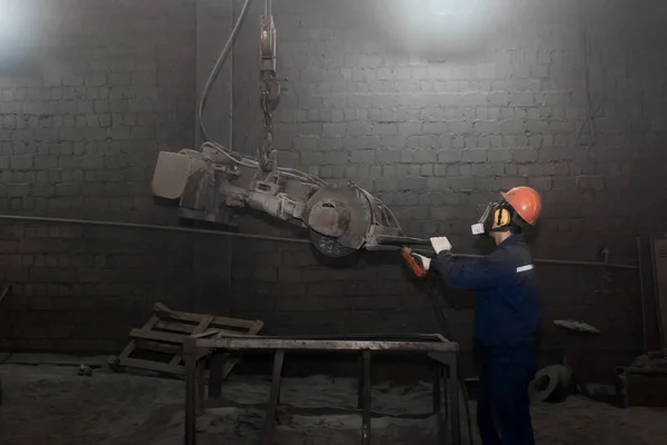 一名穿着工作服 戴防护头盔和呼吸器的工人控制着工厂车间清洗铸铁钢管的重型设备 — 图库照片