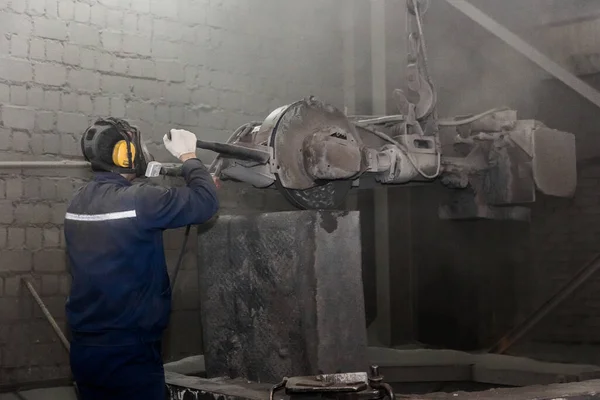 作業服を着た男と呼吸器は 産業プラントの汚れた店で鋳鉄コンクリートチューブをきれいにし 準備するために砥石で重い機器を駆動します — ストック写真
