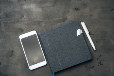 Mavi not defteri, akıllı telefon ve koyu gri masadaki kalem.