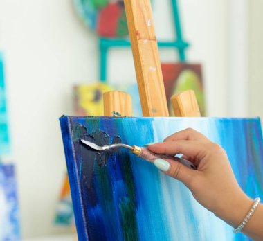 Sanat sınıfı, çizim ve yaratıcılık konsepti - Palet ve boya fırçası ile şövale önünde oturan kız öğrenci, yakın çekim