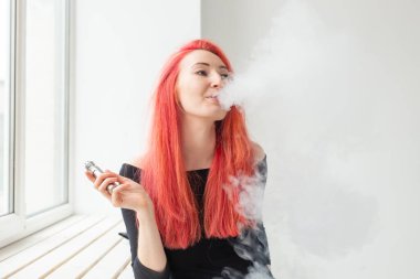 Gençlik ve bağımlılık kavramı - genç kızıl saçlı kadın pencere yakınında vape sigara