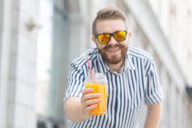 Elinde taze portakal suyu tutan sakallı ve bıyıklı bulanık ve şık genç hipster erkek portresi. Sağlıklı atıştırmalık konsepti.