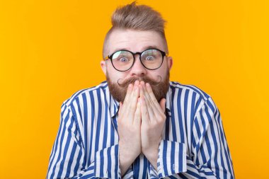 Gözlüklü şaşıran genç erkek hipster ağzını kapatır ve sarı bir arka plan üzerinde poz güler. Çizim ve sürpriz kavramı.