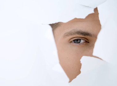 Genç işadamı kağıt duvardaki delikten bakıyor.