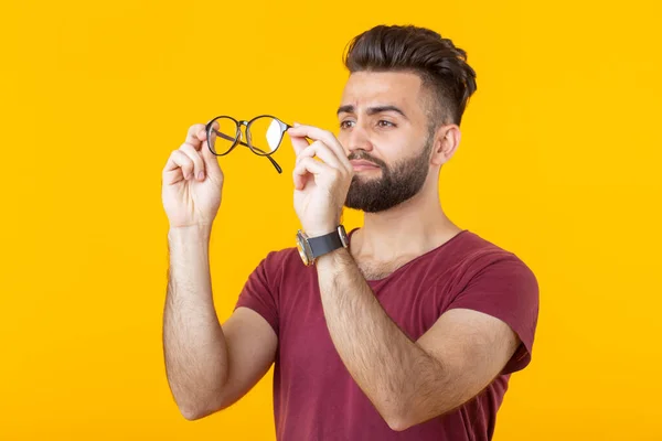 Sarı Bir Arka Planda Ayakta Iken Genç Yakışıklı Adam Gözlüklerini — Stok fotoğraf
