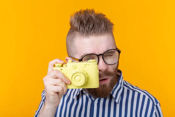 口ひげとあごひげを持つかわいい若い男性カメラマンは 黄色の背景に黄色のヴィンテージカメラを撮影しています 趣味と仕事の概念 — ストック写真