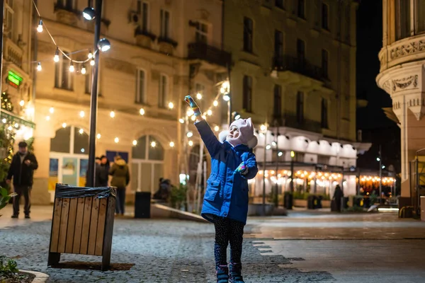 Sokak Lambalarıyla Aydınlatılmış Küçük Bir Kız Arka Planda Noel Süsü — Stok fotoğraf