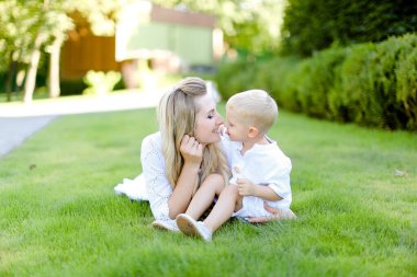 Young mother sitting with little baby on grass in yard.
