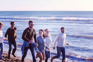 Sonbahar günü plajda koşan bir grup arkadaş