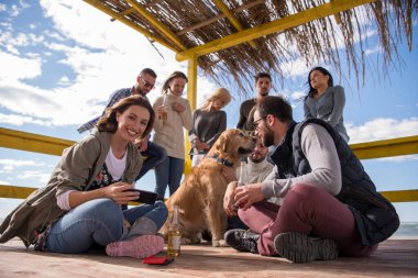 Bir grup arkadaş, sonbahar günü kumsalda eğleniyorlar.