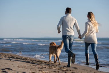 Köpekli çift, sonbahar günü sahilde eğleniyor.
