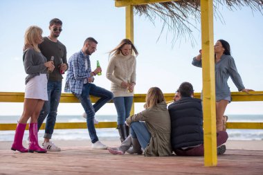 Bir grup arkadaş, sonbahar günü kumsalda eğleniyorlar.