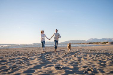 Köpekli çift, sonbahar günü sahilde eğleniyor.