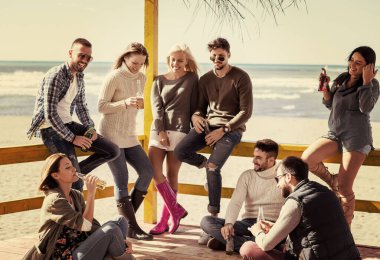 Bir grup arkadaş, sonbahar günü kumsalda eğleniyorlar.