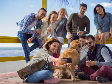 Bir grup arkadaş, sonbahar günü kumsalda eğleniyorlar.