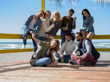 Bir grup arkadaş, sonbahar günü kumsalda eğleniyorlar.