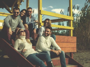 Bir grup arkadaş, sonbahar günü kumsalda eğleniyorlar.