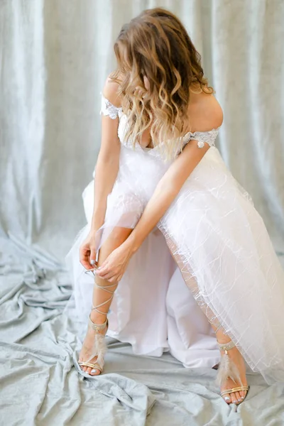 Młoda Blondynka Panna Młoda Białej Sukience Zakładająca Buty Studio Fotograficznym — Zdjęcie stockowe