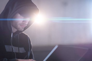 Genç yetenekli hacker karanlık ofiste çalışırken dizüstü bilgisayar kullanıyor.