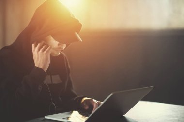 Genç yetenekli hacker karanlık ofiste çalışırken dizüstü bilgisayar kullanıyor.