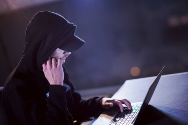 Karanlık ofiste çalışırken dizüstü bilgisayar kullanan yetenekli bir hacker.