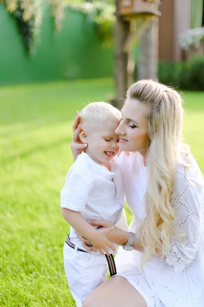 Młoda Blond Matka Siedzi Dzieckiem Trawie Podwórku Całuje Małego Chłopca — Zdjęcie stockowe