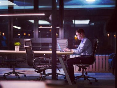 karanlık ofiste dizüstü bilgisayarda çalışan adam