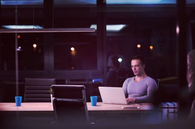 karanlık ofiste dizüstü bilgisayarda çalışan adam