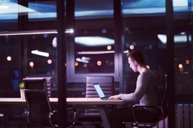 karanlık ofiste dizüstü bilgisayarda çalışan adam