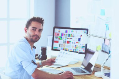 İnternette çalışırken bilgisayarın ve dizüstü bilgisayarın önünde grafik stüdyosunda oturan genç tasarımcının portresi.