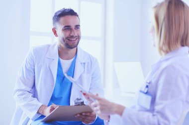 Yakışıklı doktor genç bayan doktorla konuşuyor ve ofisinde otururken notlar alıyor..