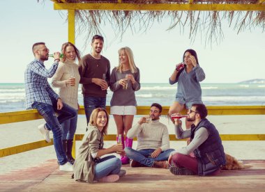 Bir grup arkadaş, sonbahar günü kumsalda eğleniyorlar.