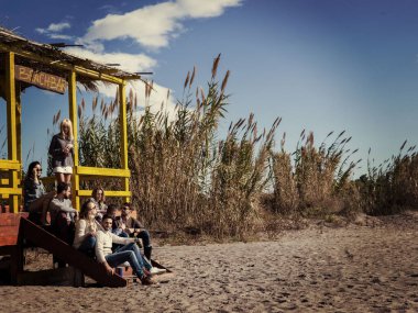 Bir grup arkadaş, sonbahar günü kumsalda eğleniyorlar.