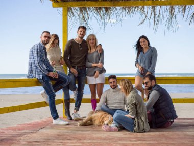 Bir grup arkadaş, sonbahar günü kumsalda eğleniyorlar.