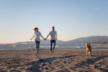 Köpekli çift, sonbahar günü sahilde eğleniyor.