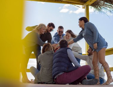 Bir grup arkadaş, sonbahar günü kumsalda eğleniyorlar.