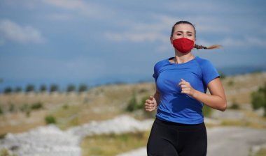 Kırsalda koşan koruyucu maskeli bir kadın.