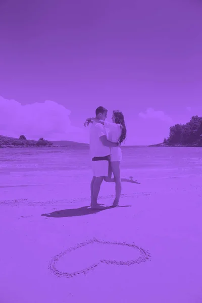 恋のカップルは砂の上にハートの絵を描くとビーチで楽しんでいます — ストック写真