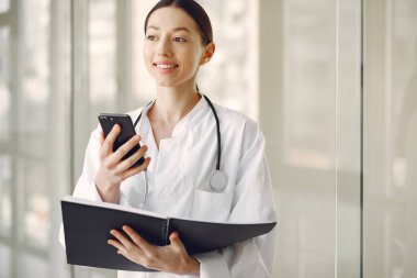 Beyaz üniformalı kadın doktor koridorda dikiliyor.