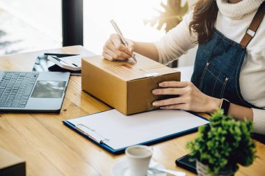 İş sahipleri paket kutularına yazmak için kalem ve paketlenmiş kutuları hazırlamak için çevrimiçi siparişleri kontrol etmek için bilgisayar kullanırlar. Müşterilere dağıtım için ürünleri paketle.