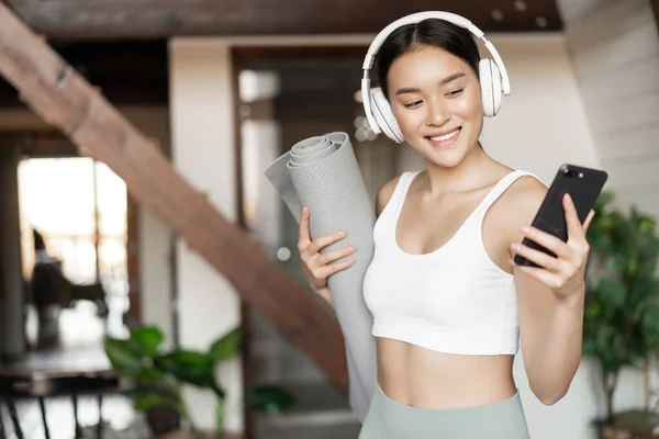Sonriente Chica Asiática Con Auriculares Mirando Teléfono Móvil Celebración Alfombra —  Fotos de Stock